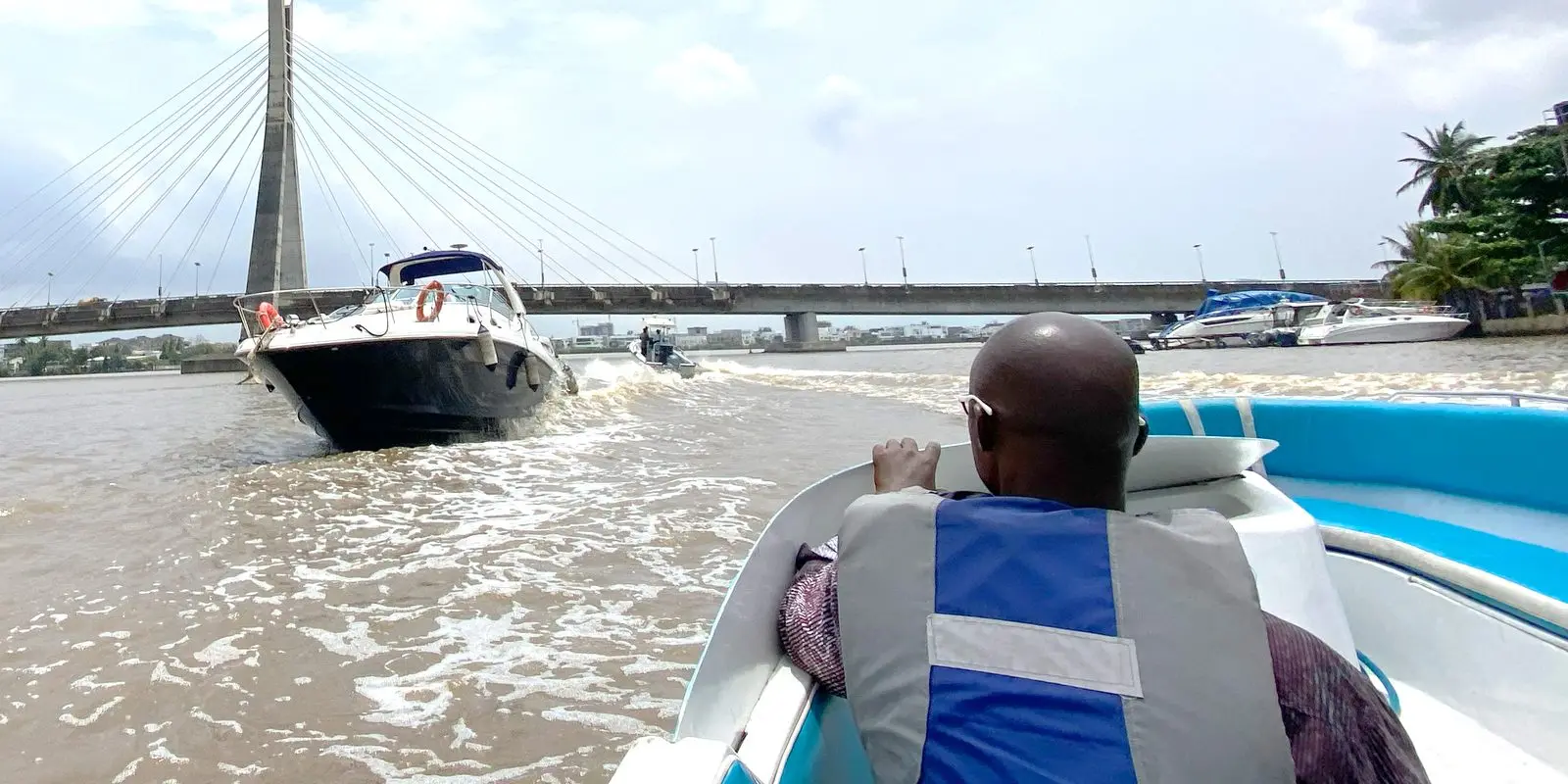 A guest in a life jacket aboard a boat on Lagos Lagoon, heading under the Lekki–Ikoyi Link Bridge